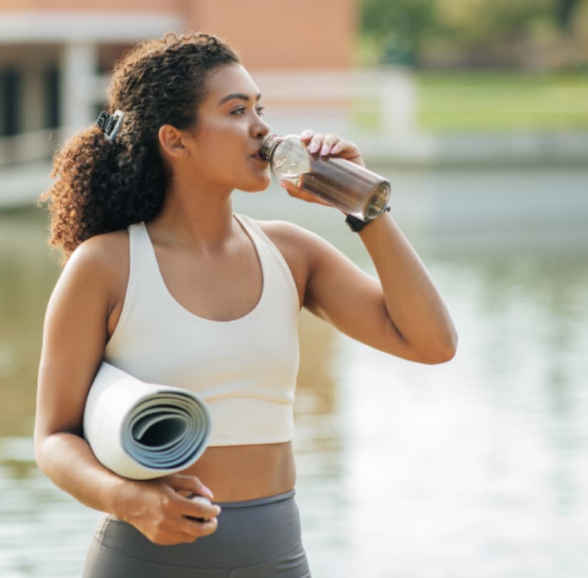 A woman with a yoga mat drinking water