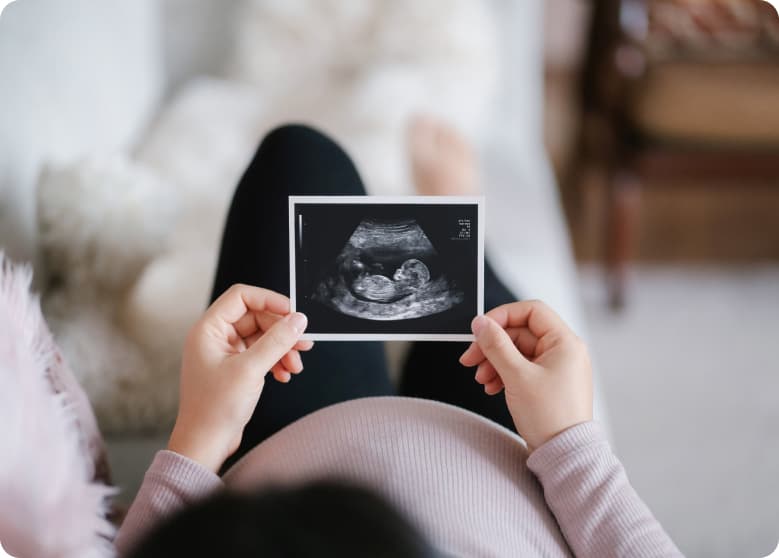 A pregnant person holding a sonogram of their child